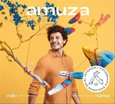 Un hombre con cabello rizado sonríe, en medio de coloridas obras de arte, sobre un fondo amarillo.
