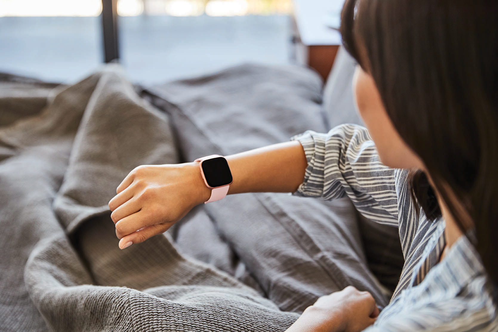 Frau im gestreiften Hemd, die eine rosa Smartwatch an ihrem Handgelenk überprüft.