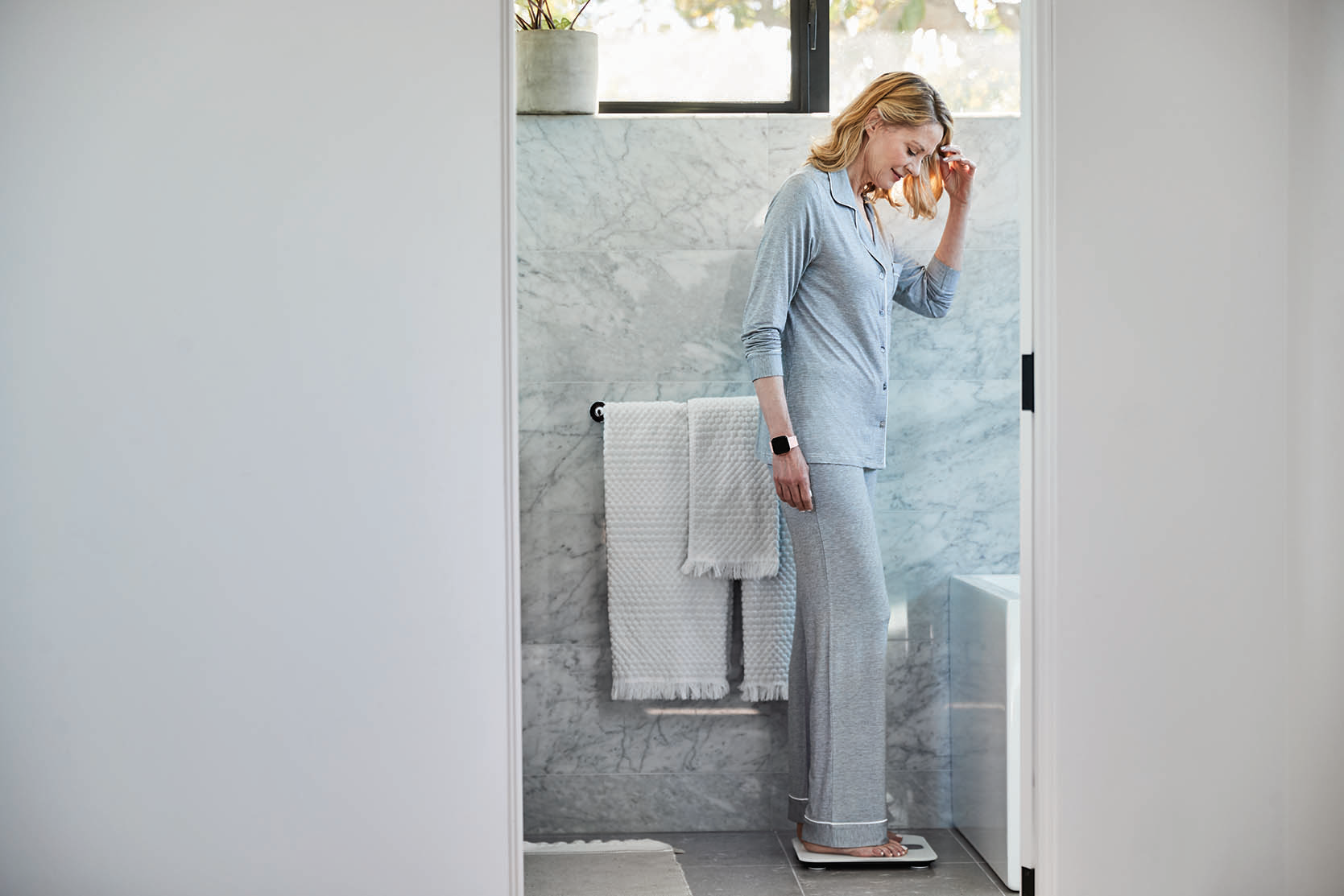 Frau im Pyjama steht auf einer Waage im Badezimmer und schaut nach unten.