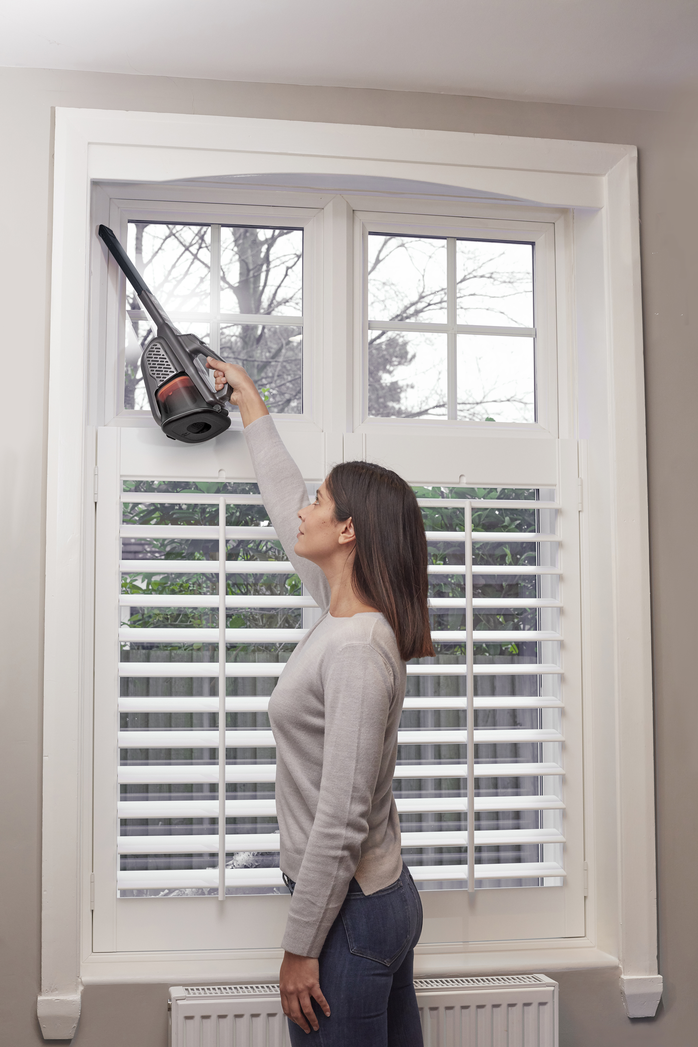 Frau putzt Fenster mit Staubsauger. Weißer Fensterrahmen, Fensterläden.