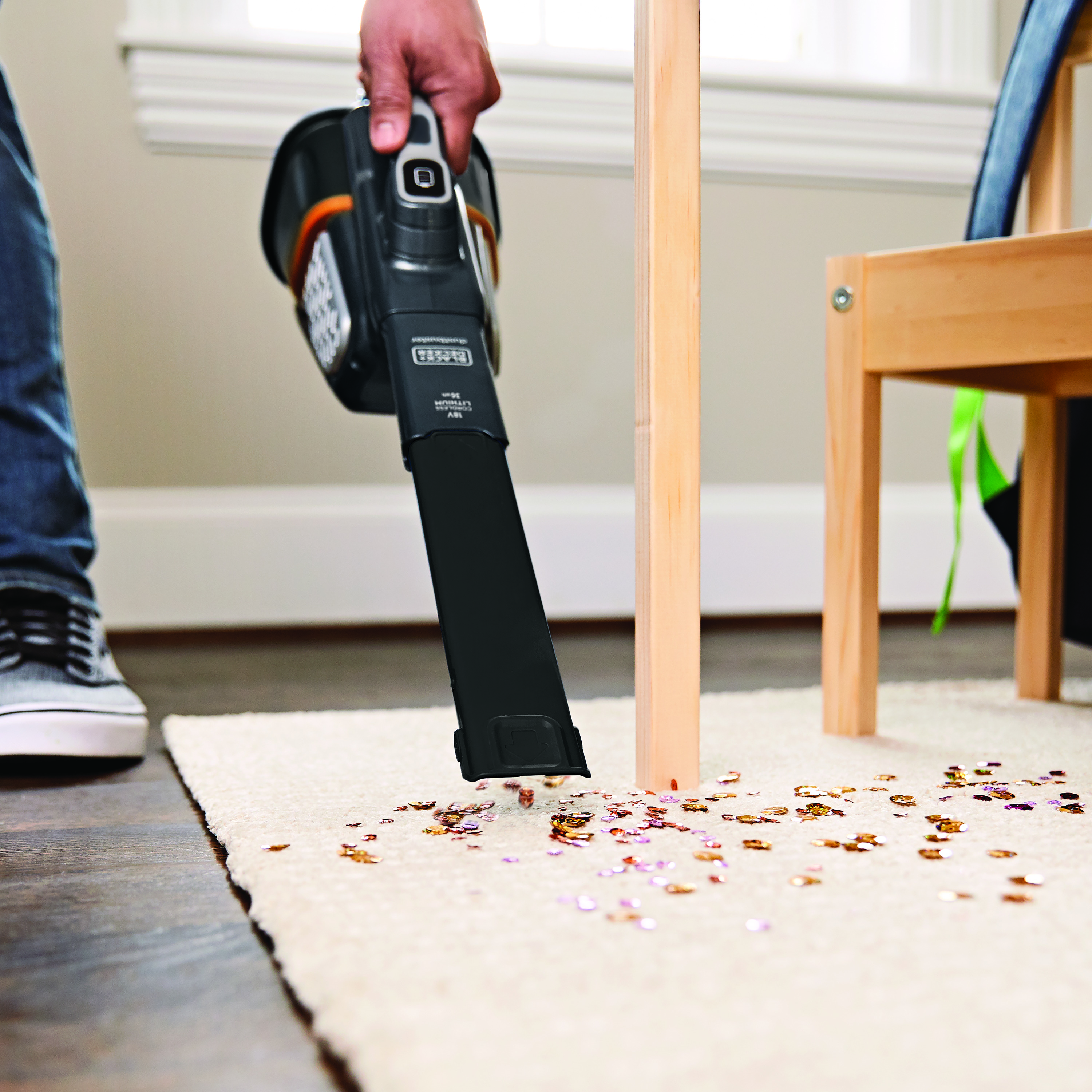 Person saugt einen Teppich mit einem Handstaubsauger, auf dem Konfetti verstreut ist.