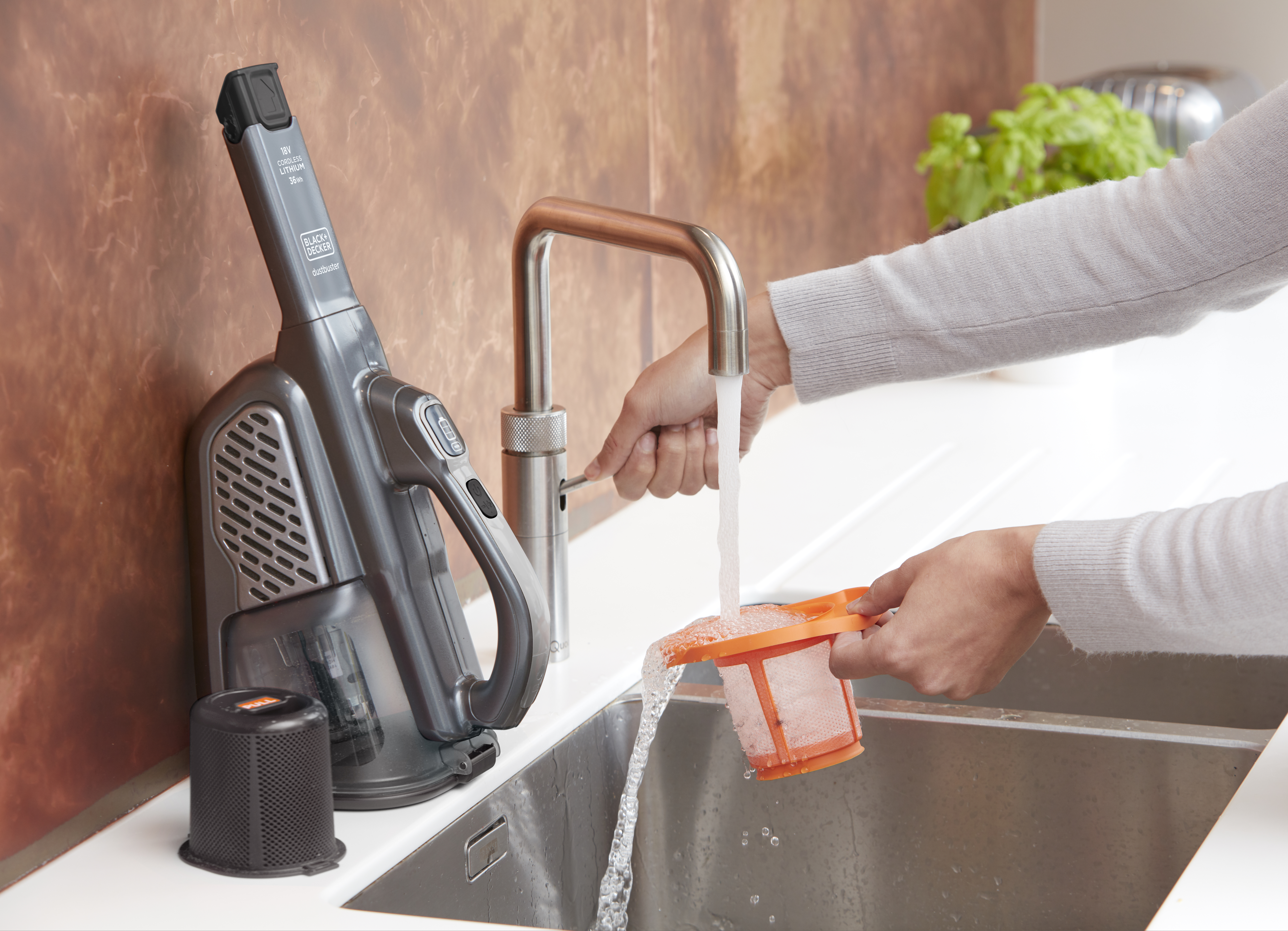 Eine Person spült einen Staubsaugerfilter unter fließendem Wasser. Der Wasserhahn ist chrom.