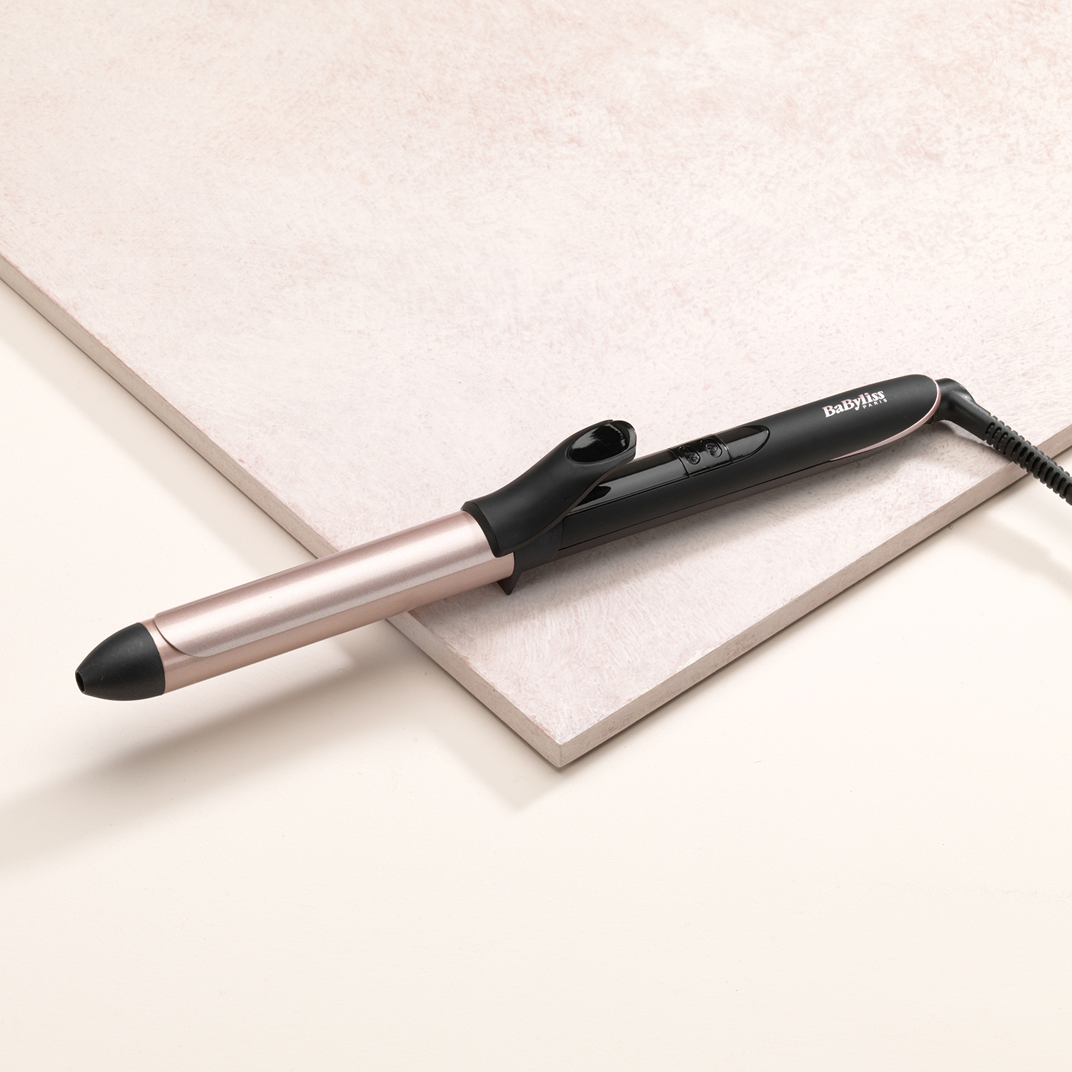 Black and rose gold curling iron on a pink and white surface.