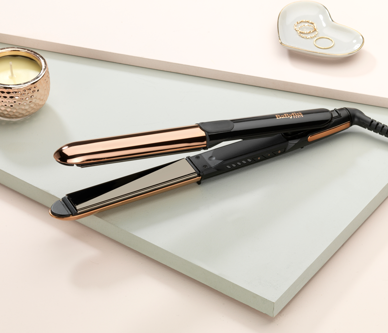 Piastra per capelli, nera e oro rosa, con una candela e un piatto a forma di cuore con anelli.