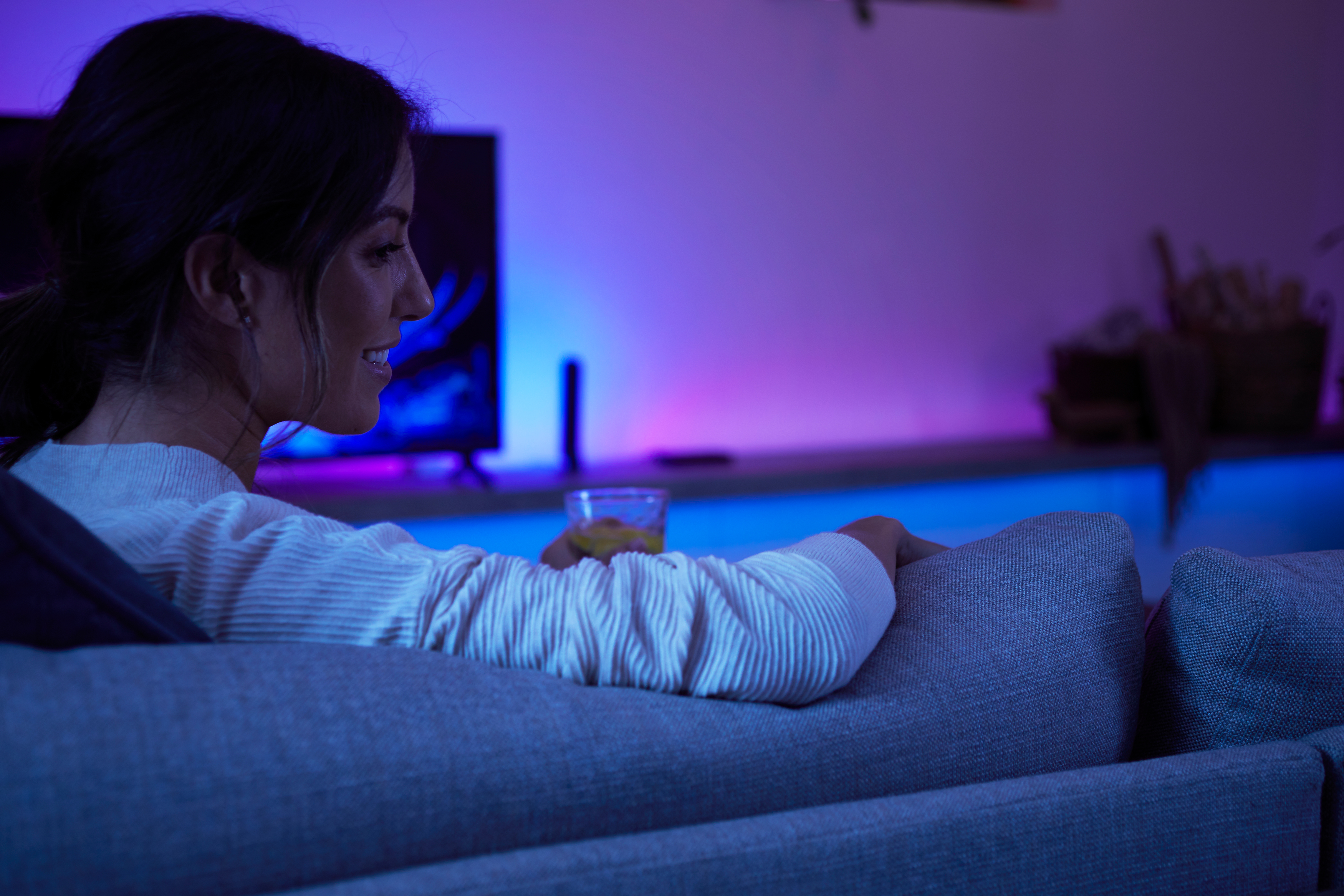 Frau auf einem Sofa, die das Licht eines Fernsehers und farbige Lichtstreifen genießt.