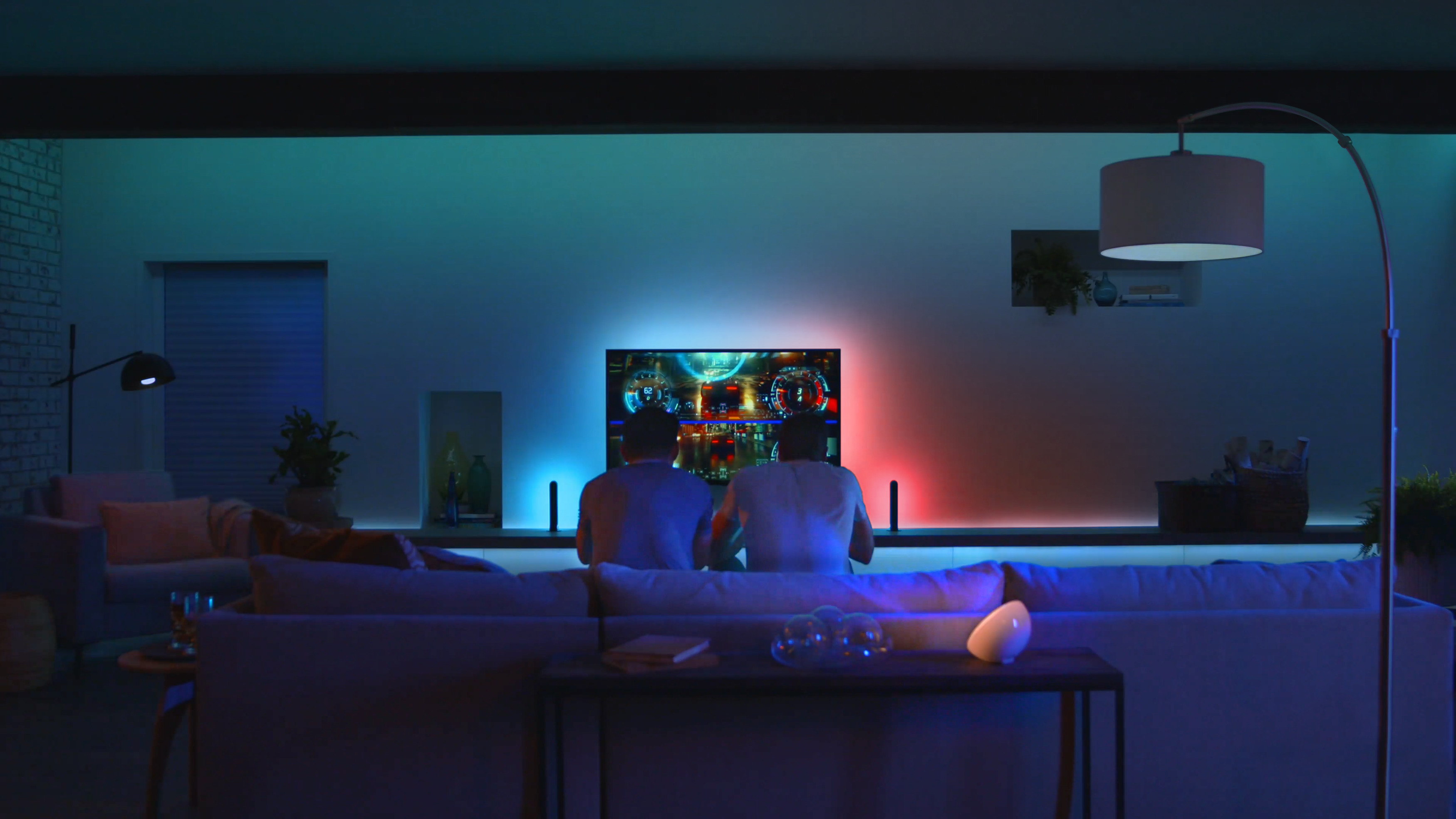 Zwei Personen spielen ein Spiel auf einem Fernseher mit farbigem Licht.