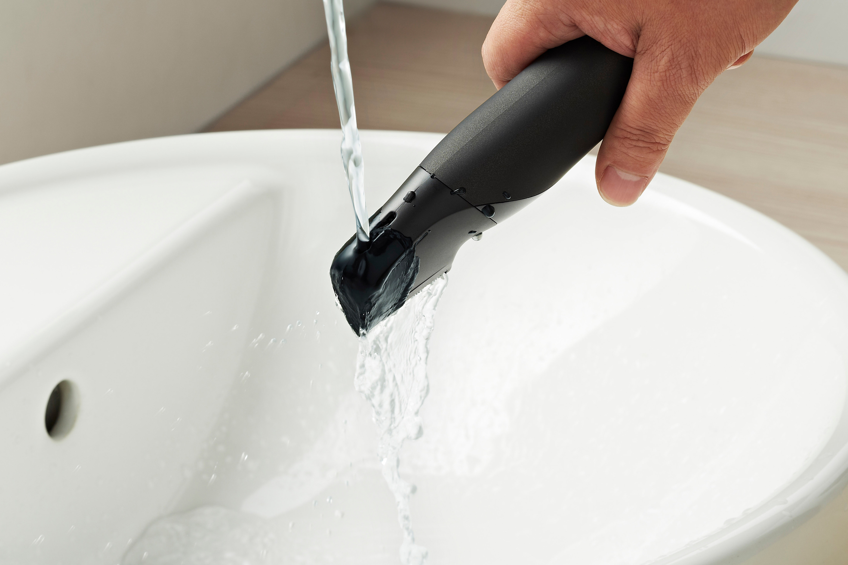 Ein schwarzes Rasiergerät unter fließendem Wasser in einem weißen Waschbecken.