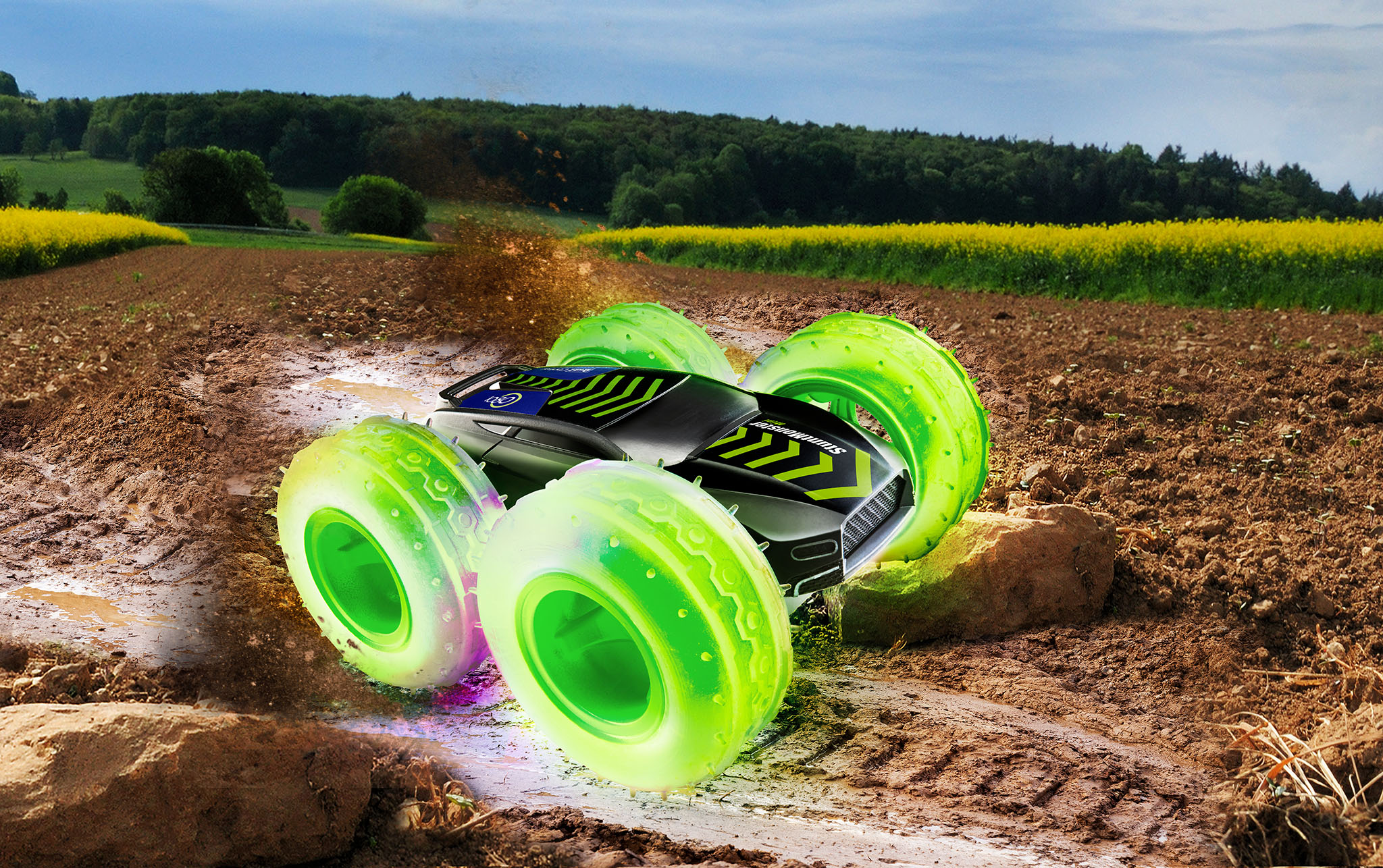 Ein Spielzeugauto mit grünen Rädern fährt durch Schlamm auf einem Feld.