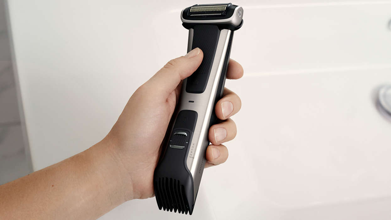 Main tenant une tondeuse à barbe argentée et noire au-dessus d'un lavabo blanc.