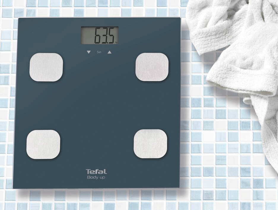 Digital bathroom scale displaying 63.5 kg with four white square foot pads.