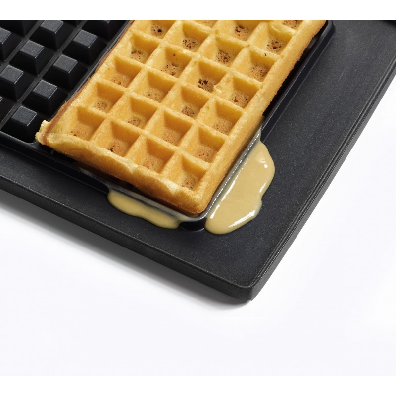 Waffle in a waffle iron, some batter is spilling over the sides.