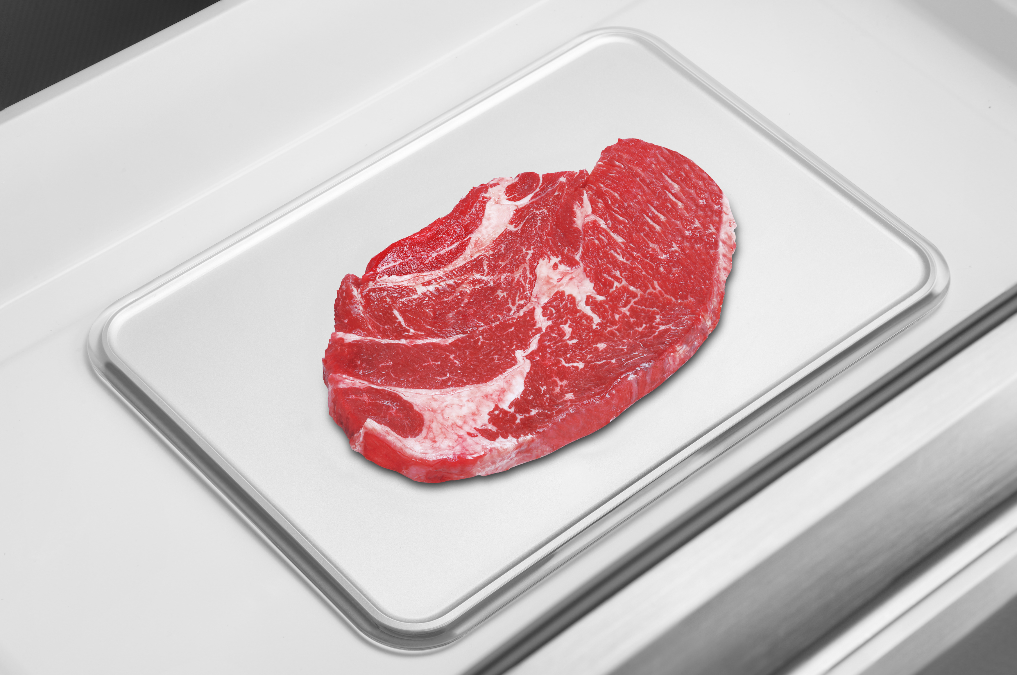 Rohes Steak auf einem weißen Tablett, platziert auf einer weißen Oberfläche. Draufsicht.