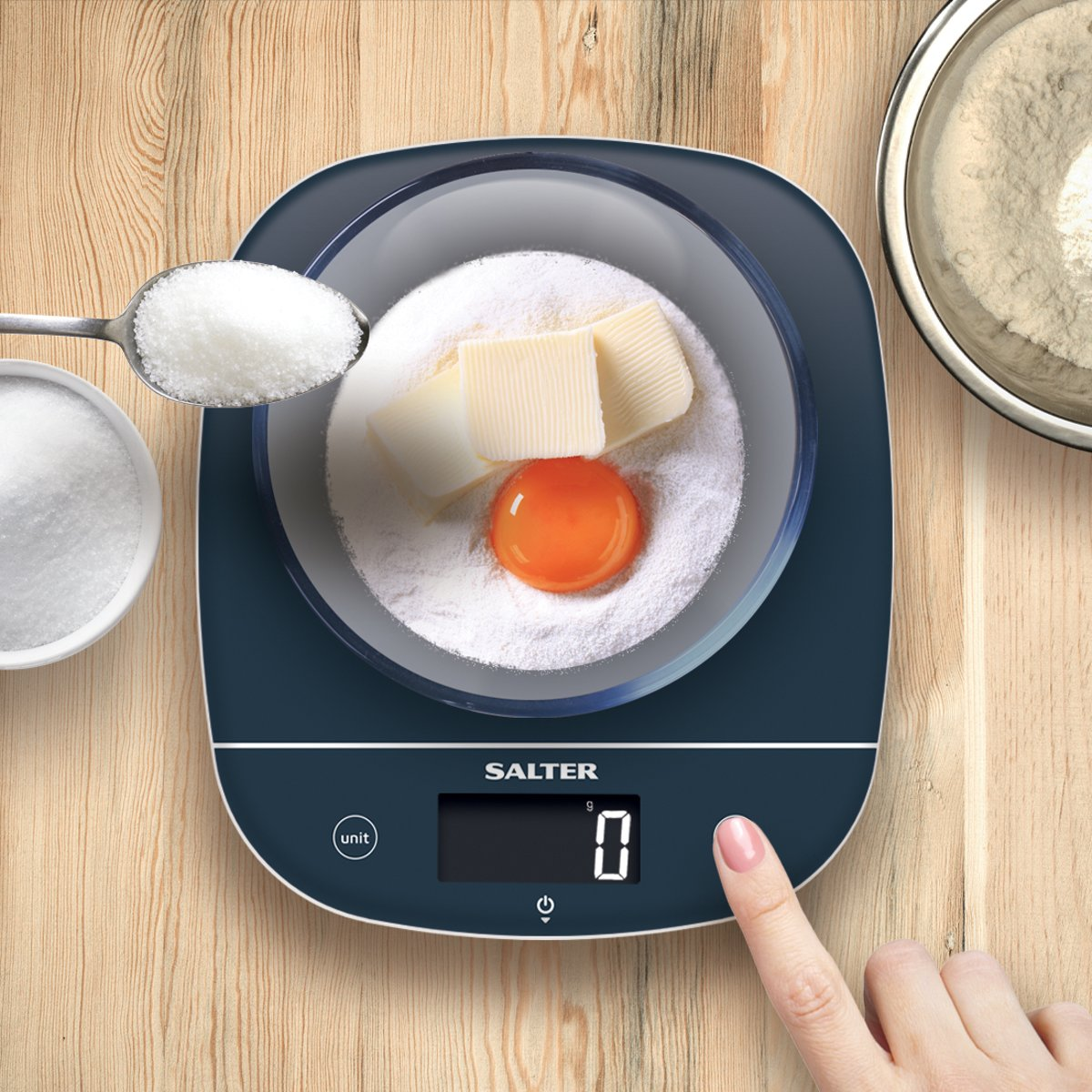 Digital kitchen scale with bowl. Sugar and butter added. Hand touching button.