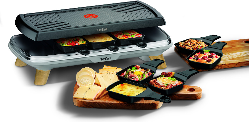 A raclette grill with cheese and various toppings. Wooden serving boards with cheese and food are included.