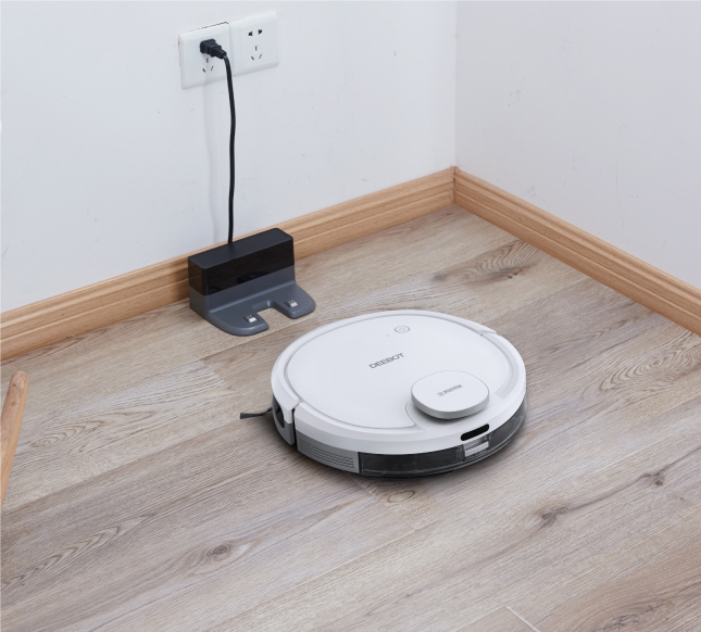 Roboter-Staubsauger auf Holzboden in der Nähe der Ladestation und der Steckdose. Das Gerät ist weiß.