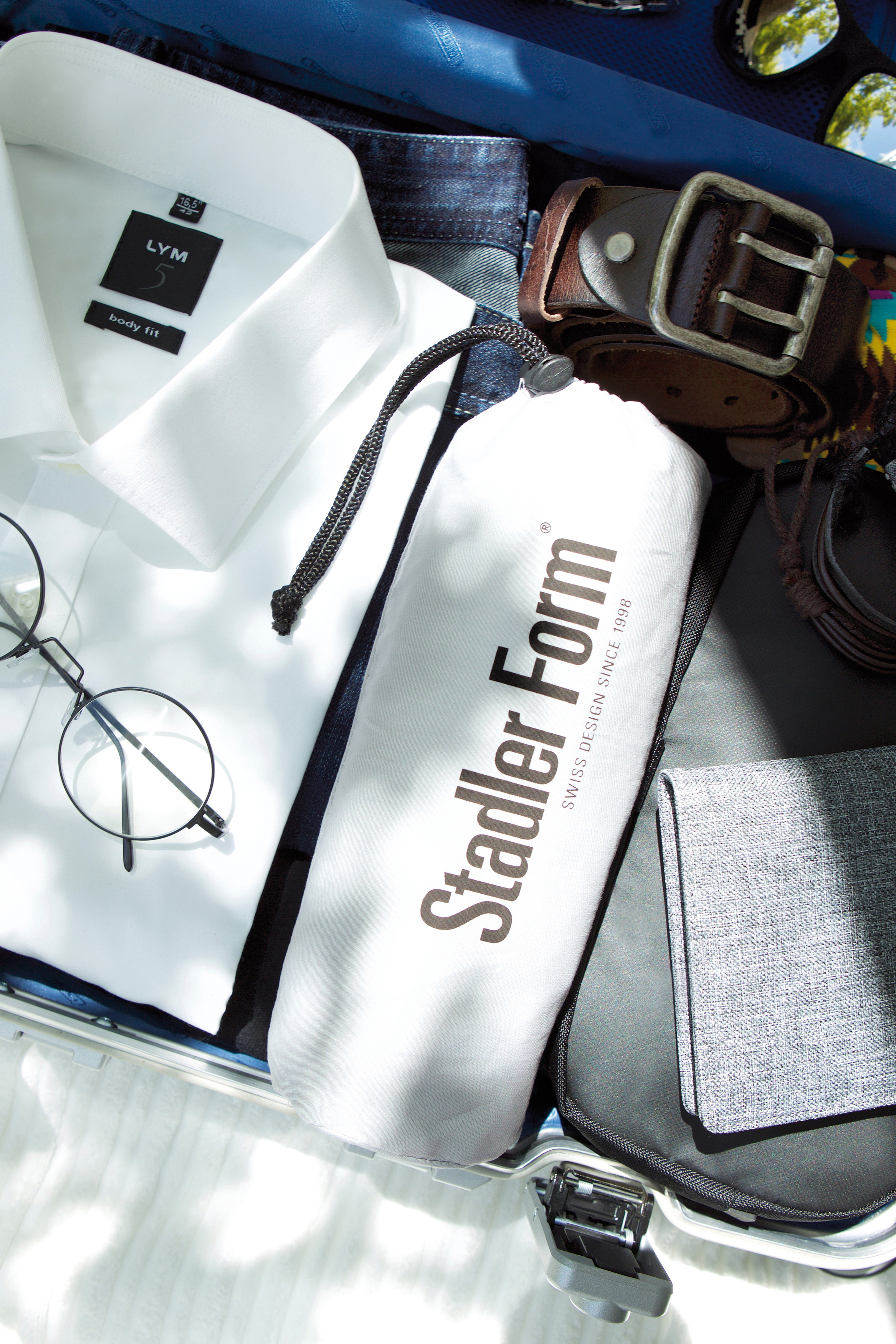 Koffer mit Kleidung und Accessoires: Hemd, Brille, Gürtel und Stadler Form Tasche.