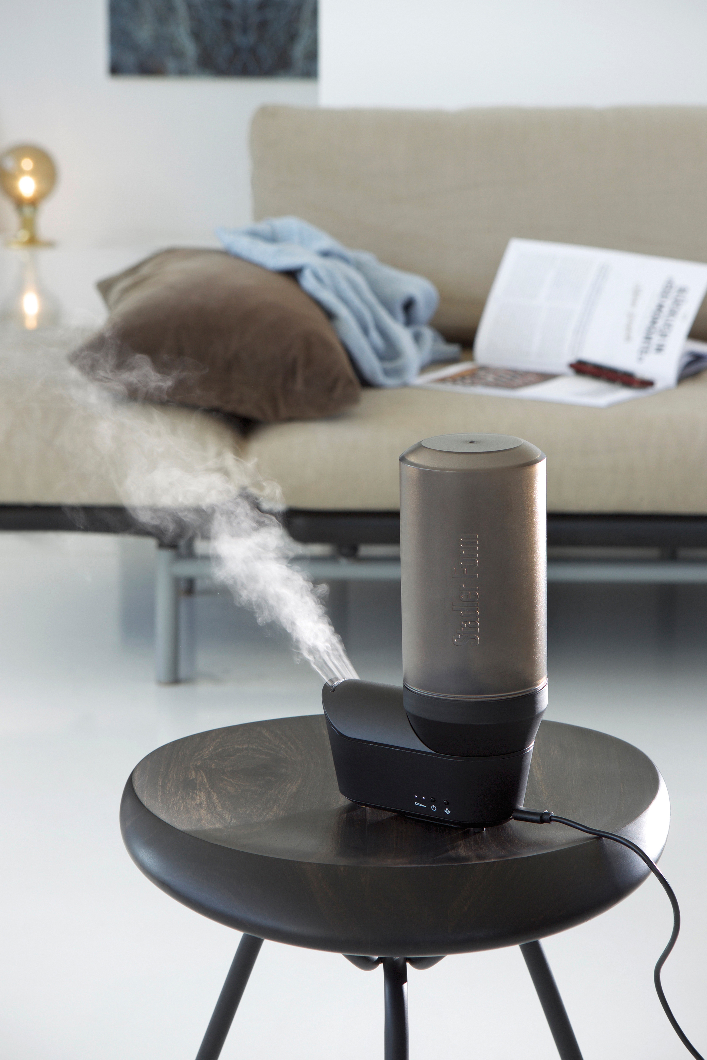 Aromadiffusor auf Holztisch, der Dampf abgibt, mit beigem Sofa im Hintergrund.