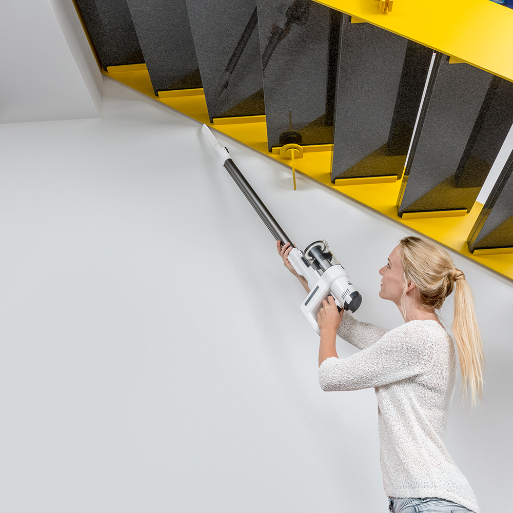 Frau reinigt Treppen mit einem weißen Staubsauger, Stufen sind gelb und grau.