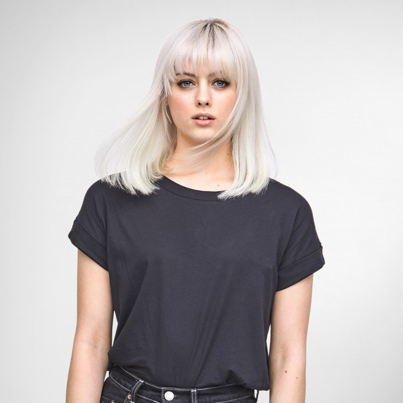 Femme blonde en t-shirt noir, fond blanc, regardant la caméra.