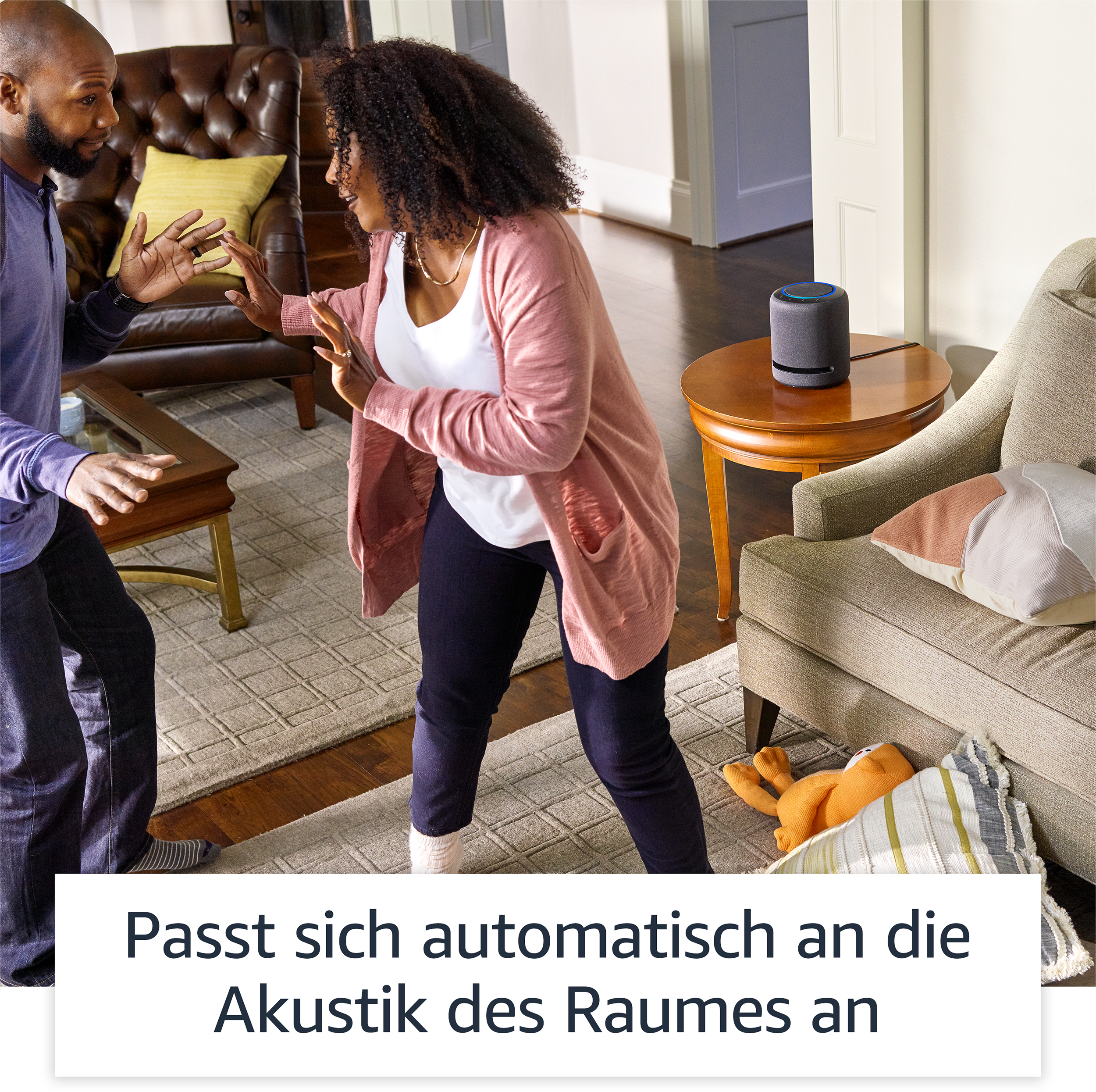 Zwei Personen interagieren in der Nähe eines Lautsprechers. Text unten.