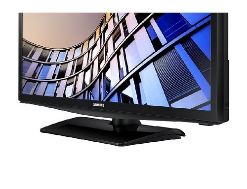Televisor negro sobre un soporte negro. La pantalla muestra una fachada de edificio moderno.