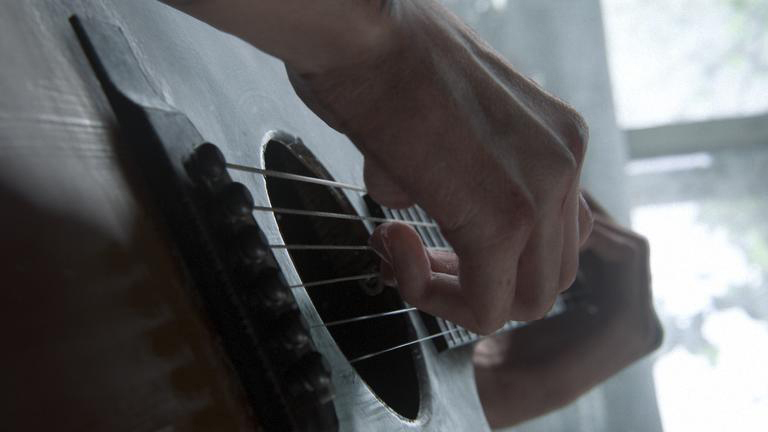 Nahaufnahme einer Hand, die Gitarre spielt. Die Finger drücken auf die Saiten.