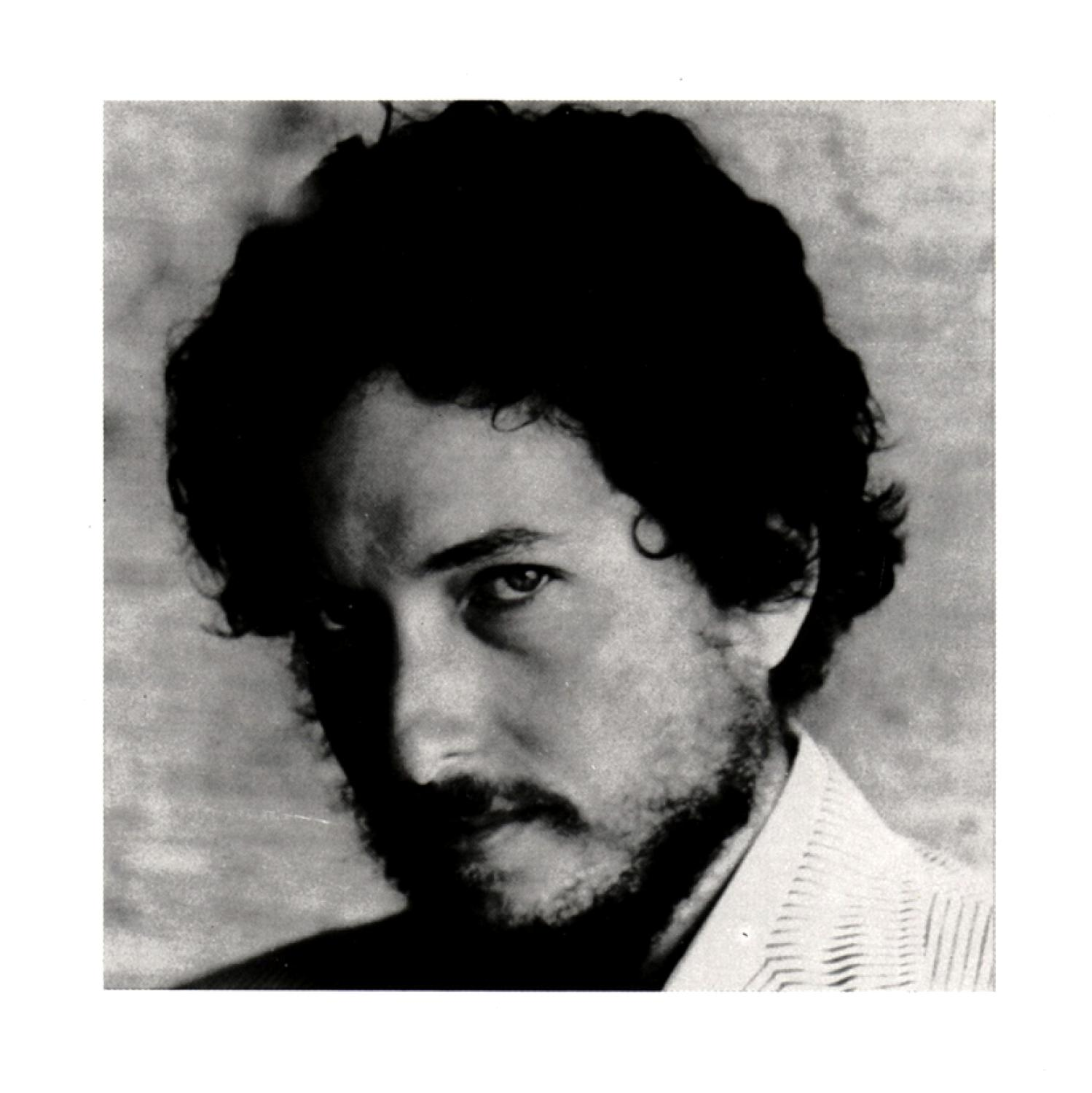 Ein Schwarz-Weiß-Porträt von Bob Dylan, der nach links blickt, mit Bart und gewelltem Haar.